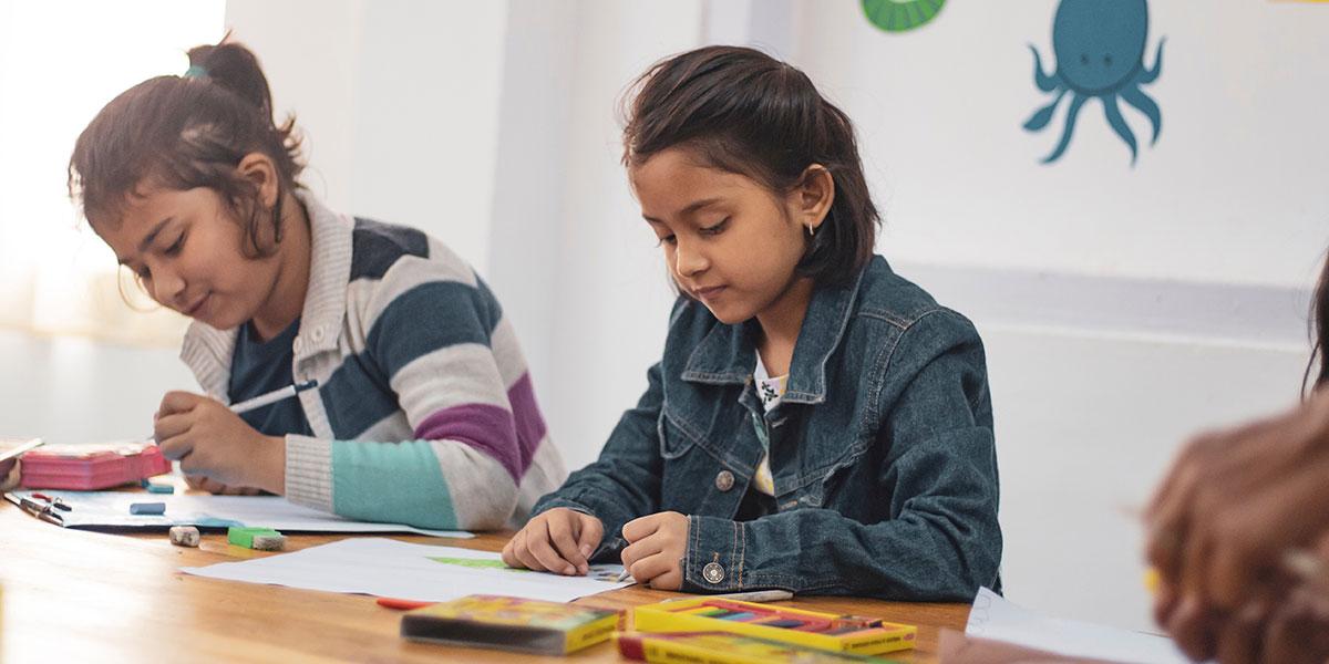 Two girls in a classroom writing.